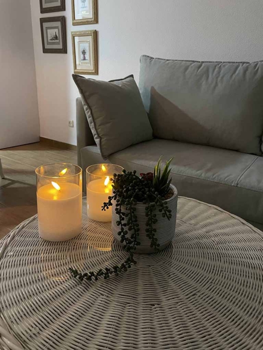 sofa gris claro mesa auxiliar blanca maceta planta velas encendidas